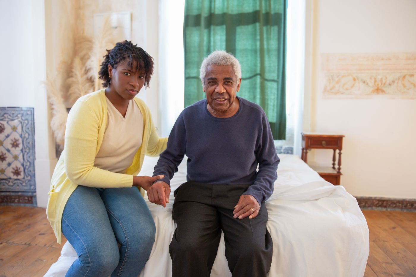 A Nigerian caregiver sitting beside a smiling older man, offering warm, attentive support at home